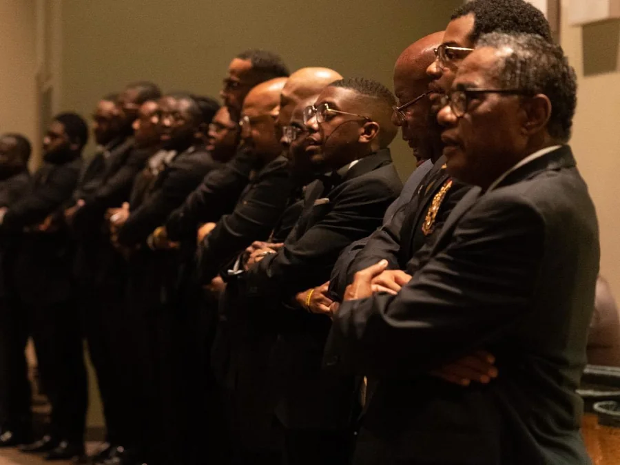 A line of brothers of the chapter in suits, shoulder to shoulder with their arms linked.