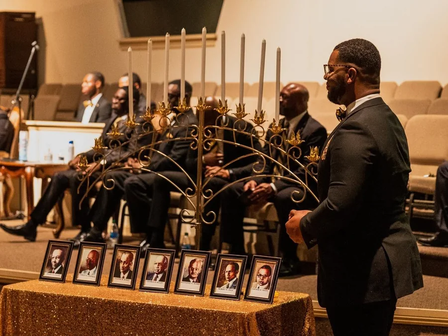 The seven framed portraits of the Jewels set out on the chapter's altar table beneath a seven-branch candelabrum, with brothers seated behind, at a Founders' Day observance in Macon.