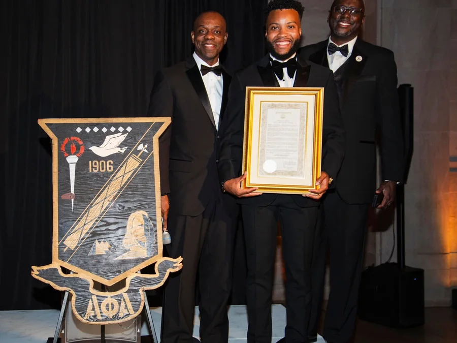 Brothers of the chapter in black tie with a framed proclamation beside the chapter banner at the seventy-fifth anniversary.
