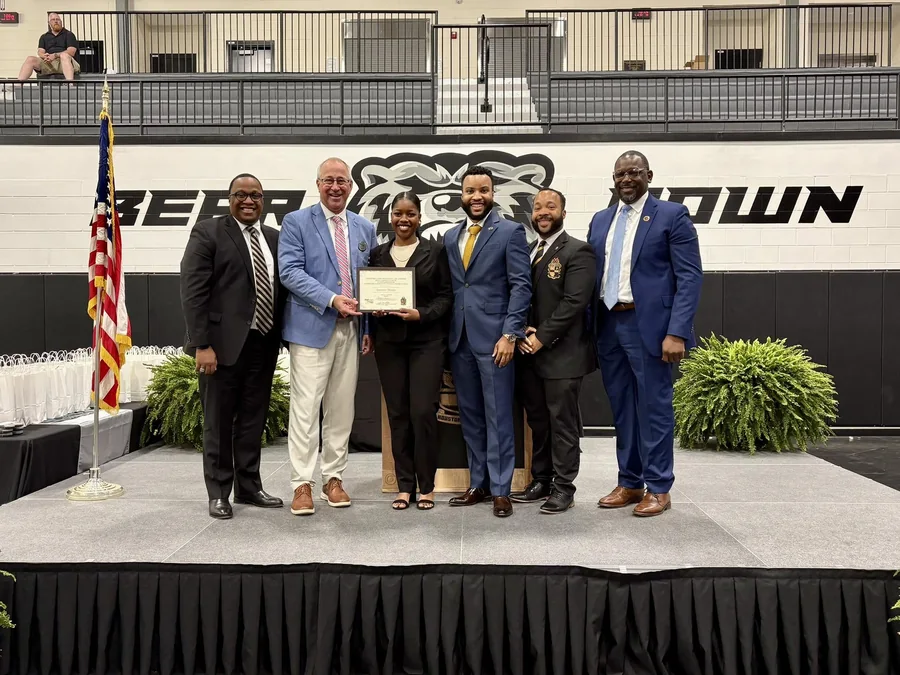 A scholarship recipient holding her award certificate with brothers of the chapter and representatives of the credit union.