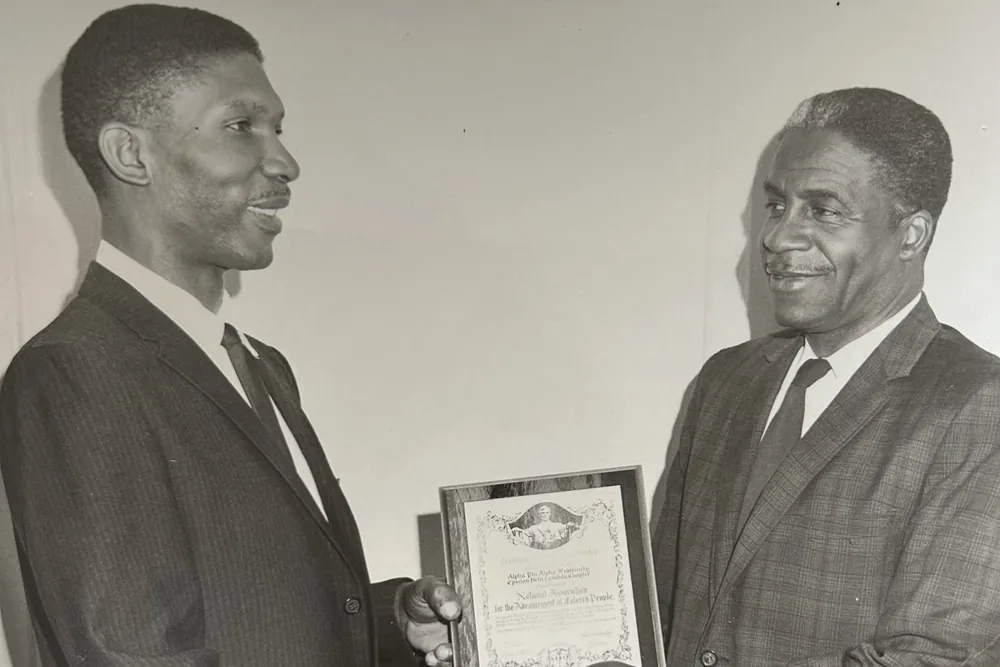 Two men in suits holding a framed certificate between them.