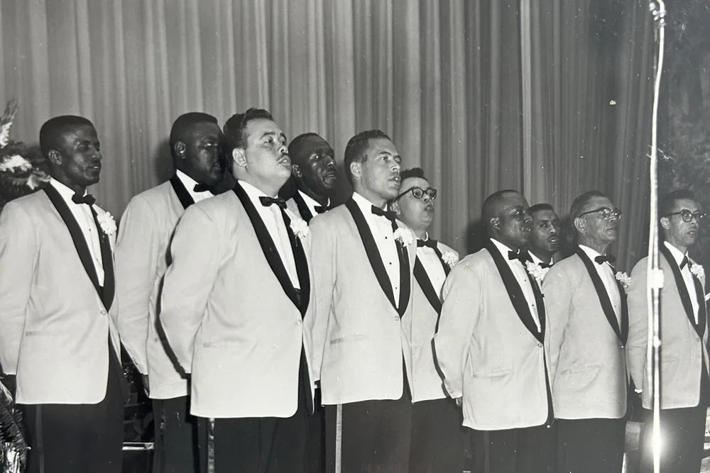 A row of men in white dinner jackets and black bow ties at a microphone on a stage.