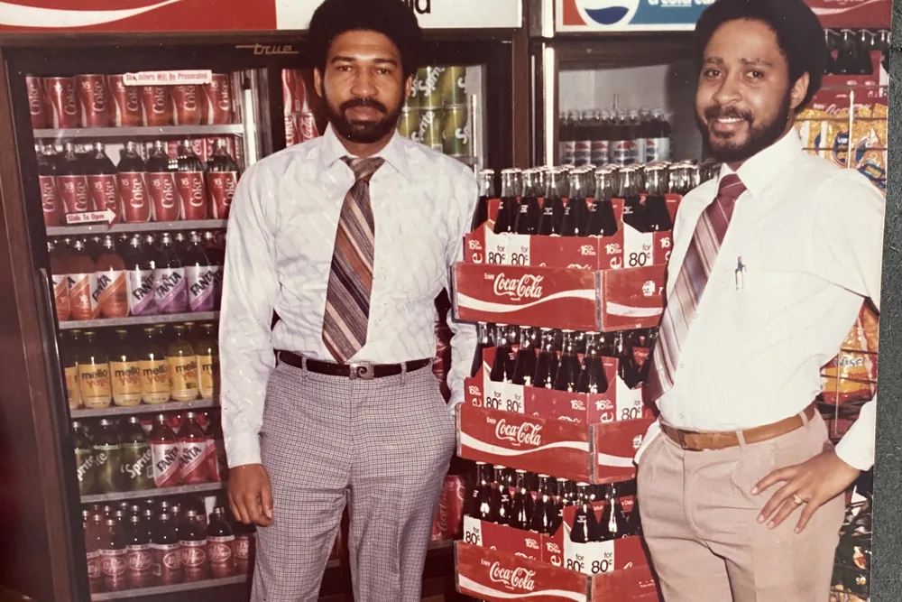 Bro. Timothy B. Jones, on the left, and Bro. Chester A. Wheeler, III, beside a stacked Coca-Cola display in a shop.