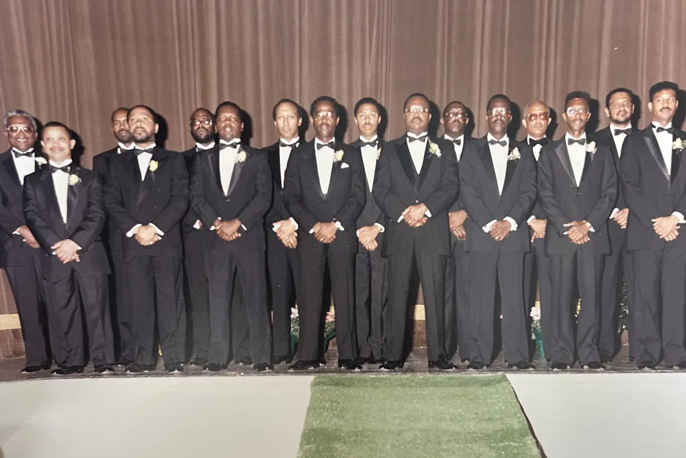 A long line of brothers in black tie, shoulder to shoulder across a hall.