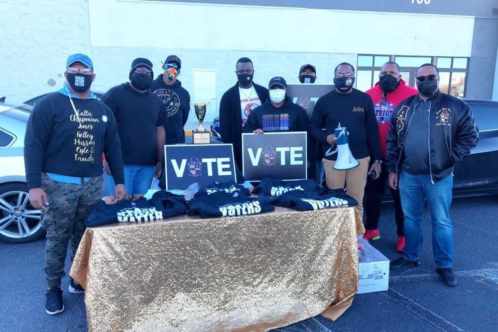 Brothers at a voter registration table under a shelter, with VOTE signs on it.