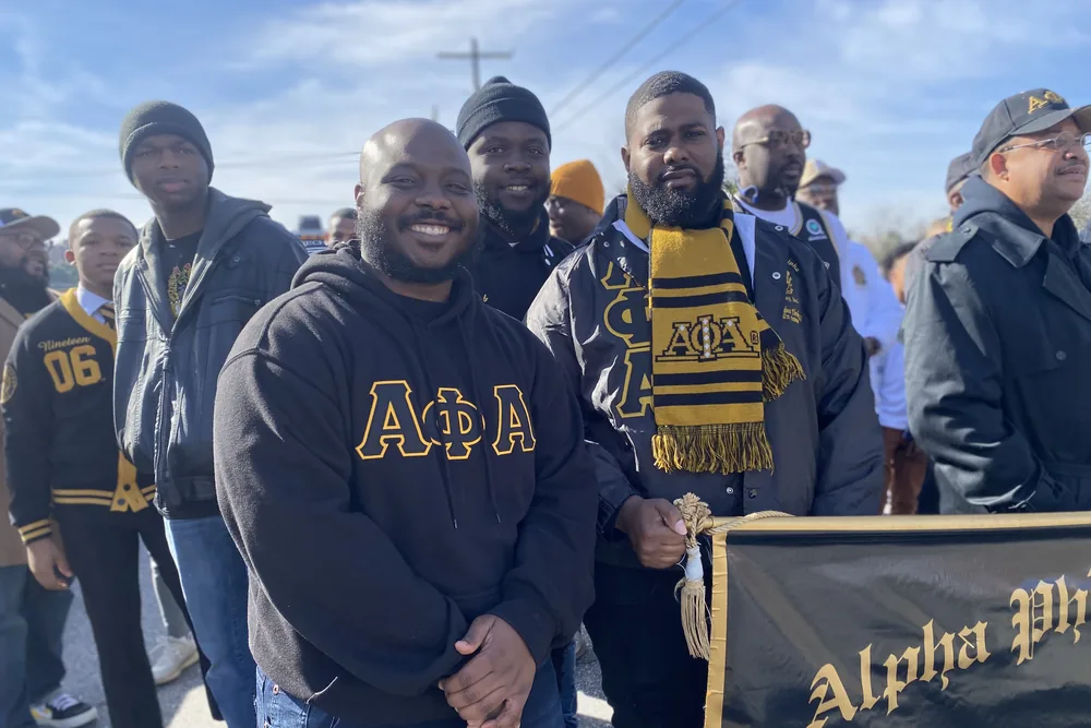 Brothers in coats and chapter jackets outdoors, holding the chapter banner.